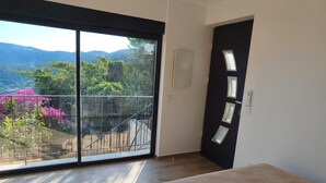 Et værelse med en stor skydedør, der fører ud til en balkon med udsigt over bjerge og blomster.