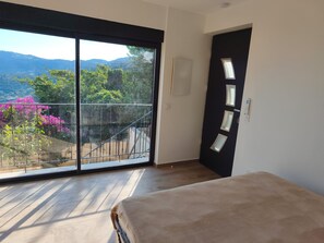 A room with a large sliding glass door leading to a balcony with a view of mountains and flowers. - House with panoramic view near Monaco (Roquebrune-Cap-Martin)