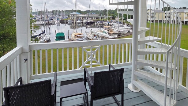A covered outdoor area with a view of a marina, featuring a white railing, a spiral staircase, and two black chairs. - Coastal Retreat w/ Balcony, Bikes & Pool Access (New Bern)