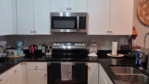 A kitchen with white cabinets, a stainless steel microwave, a black stove, and a sink. - Coastal Retreat w/ Balcony, Bikes & Pool Access (New Bern)