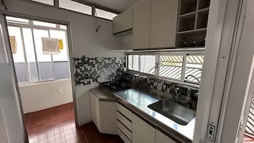 Cozinha compacta com armários brancos, bancada preta e uma janela com grade de metal.