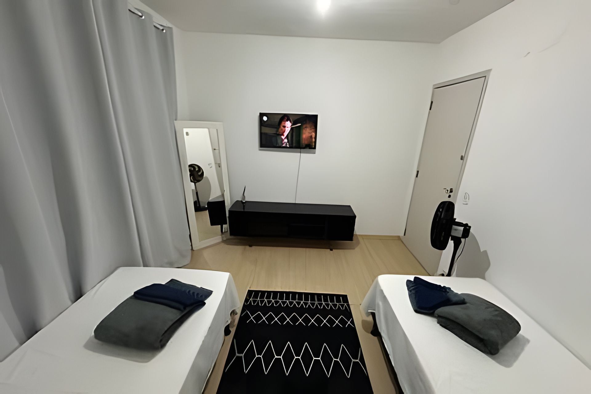 Quarto com duas camas, televisão, porta e espelho.