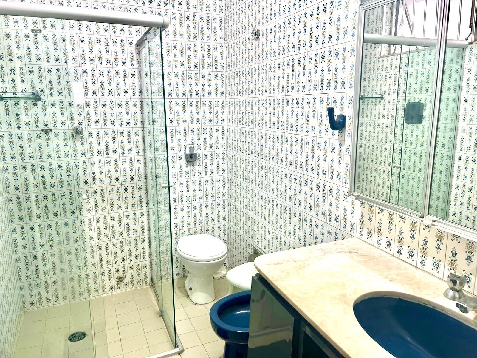 Casa de banho com azulejos estampados, cabine de chuveiro em vidro, sanita e lavatório com espelho.