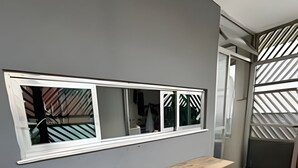 A kitchen with a wooden countertop, green chairs, a window with a view, and a patterned wall. - Quartos vila olímpia 43 (São Paulo)