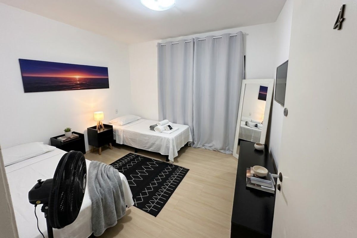 A modern hotel room with a bed, bedside table, lamp, and a view of the sunset.