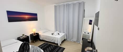 A modern hotel room with a bed, bedside table, lamp, and a view of the sunset.