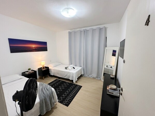 A modern hotel room with a bed, bedside table, lamp, and a view of the sunset.