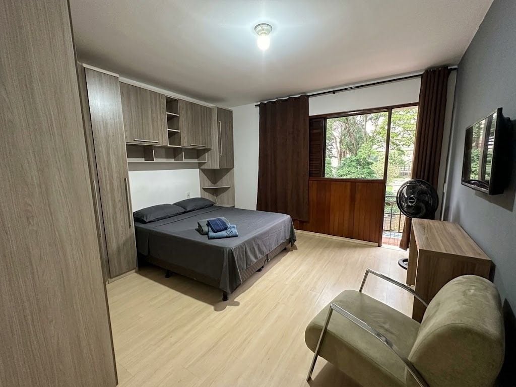 A bedroom with a bed, a desk, a chair, a wardrobe, and a window.