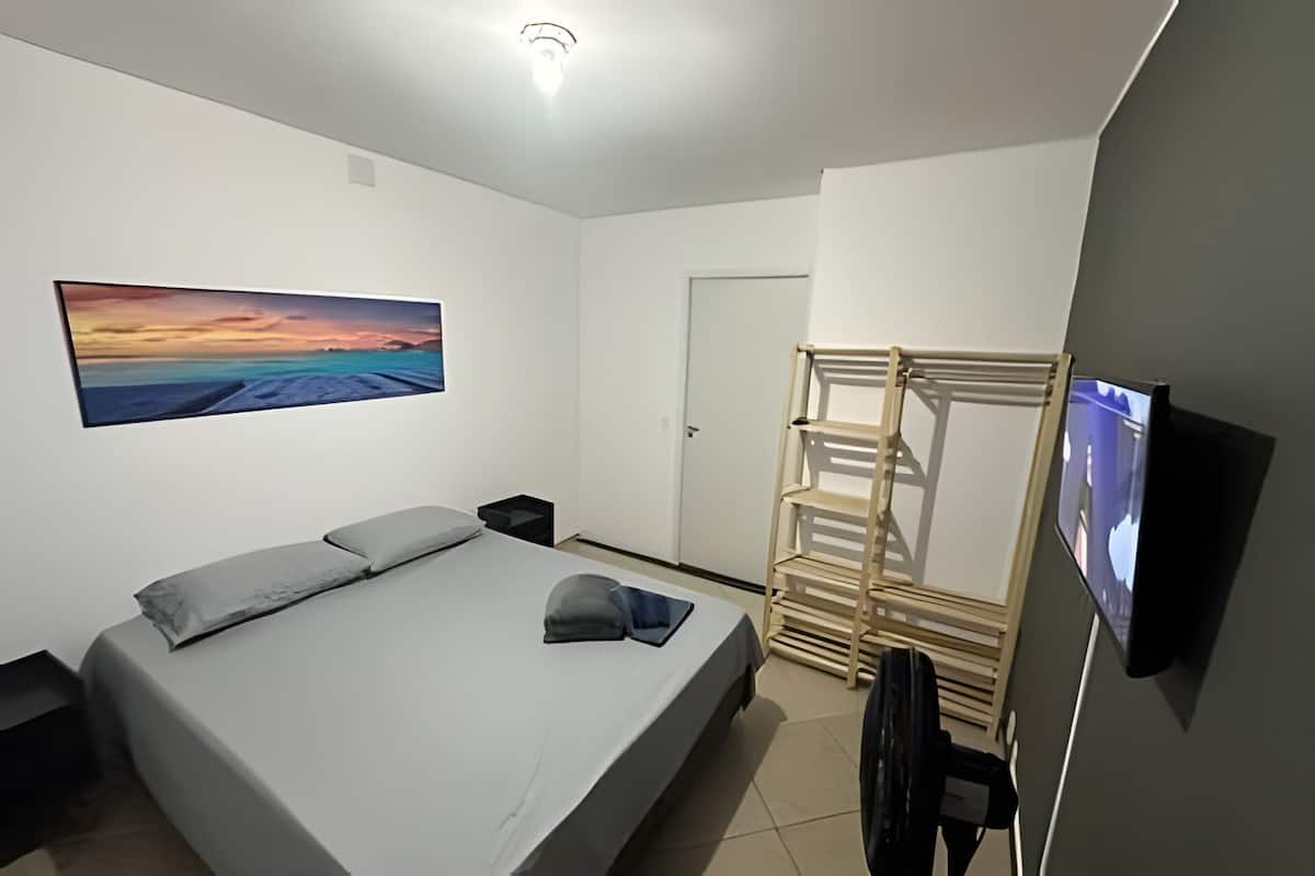 Ein Schlafzimmer mit einem Bett, einem Fernseher, einem Holzregal und einem Bild an der Wand.
