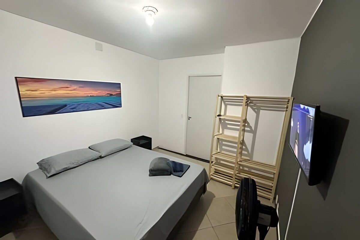 A bedroom with a bed, a TV, a wooden rack, and a painting on the wall.