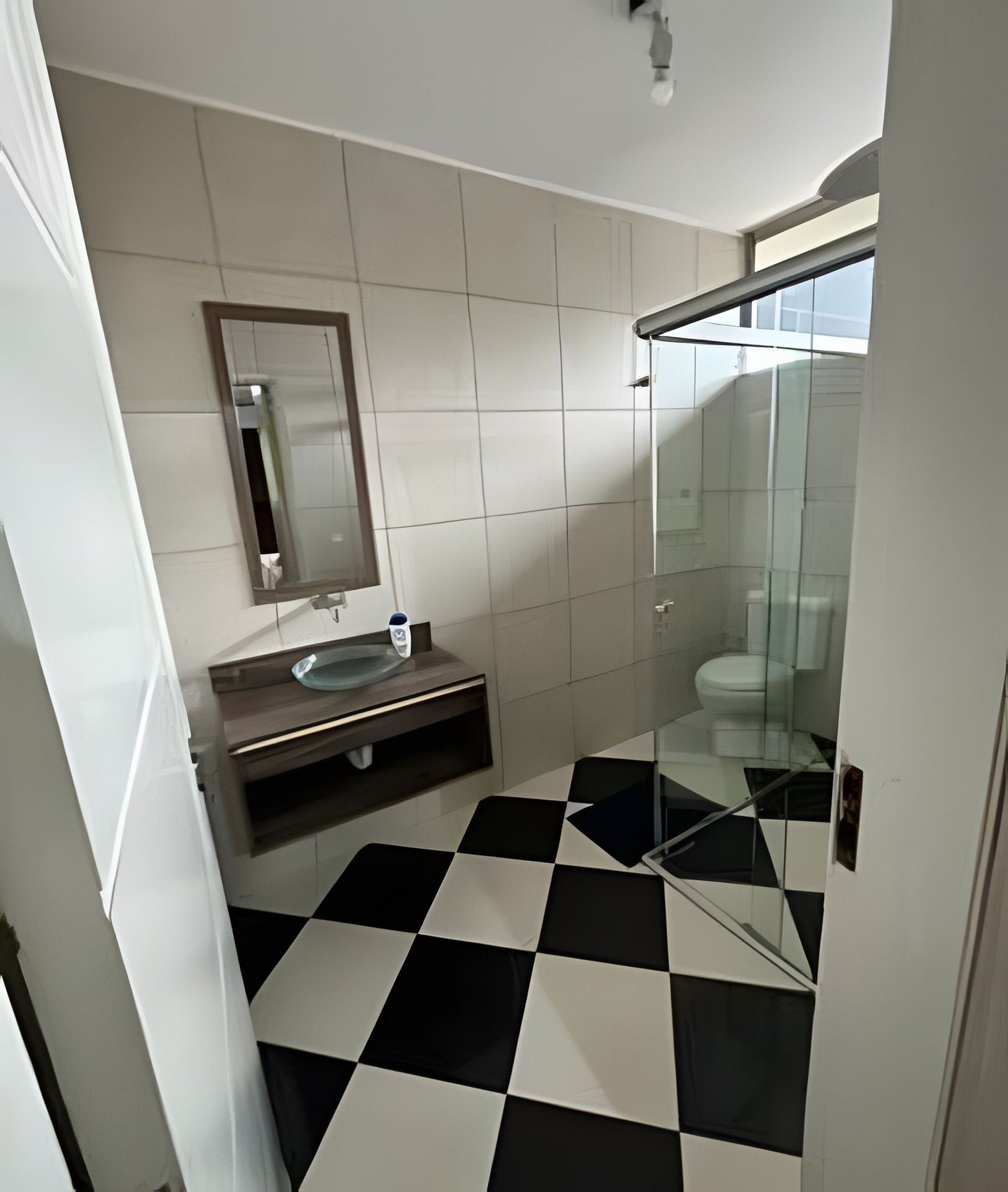 Un baño con piso a cuadros, lavamanos, espejo y cabina de ducha de vidrio.