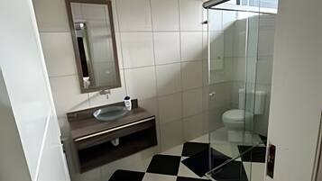 Un baño con piso a cuadros, lavamanos, espejo y cabina de ducha de vidrio.