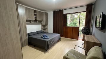 Un dormitorio con cama, escritorio, silla, armario y ventana.