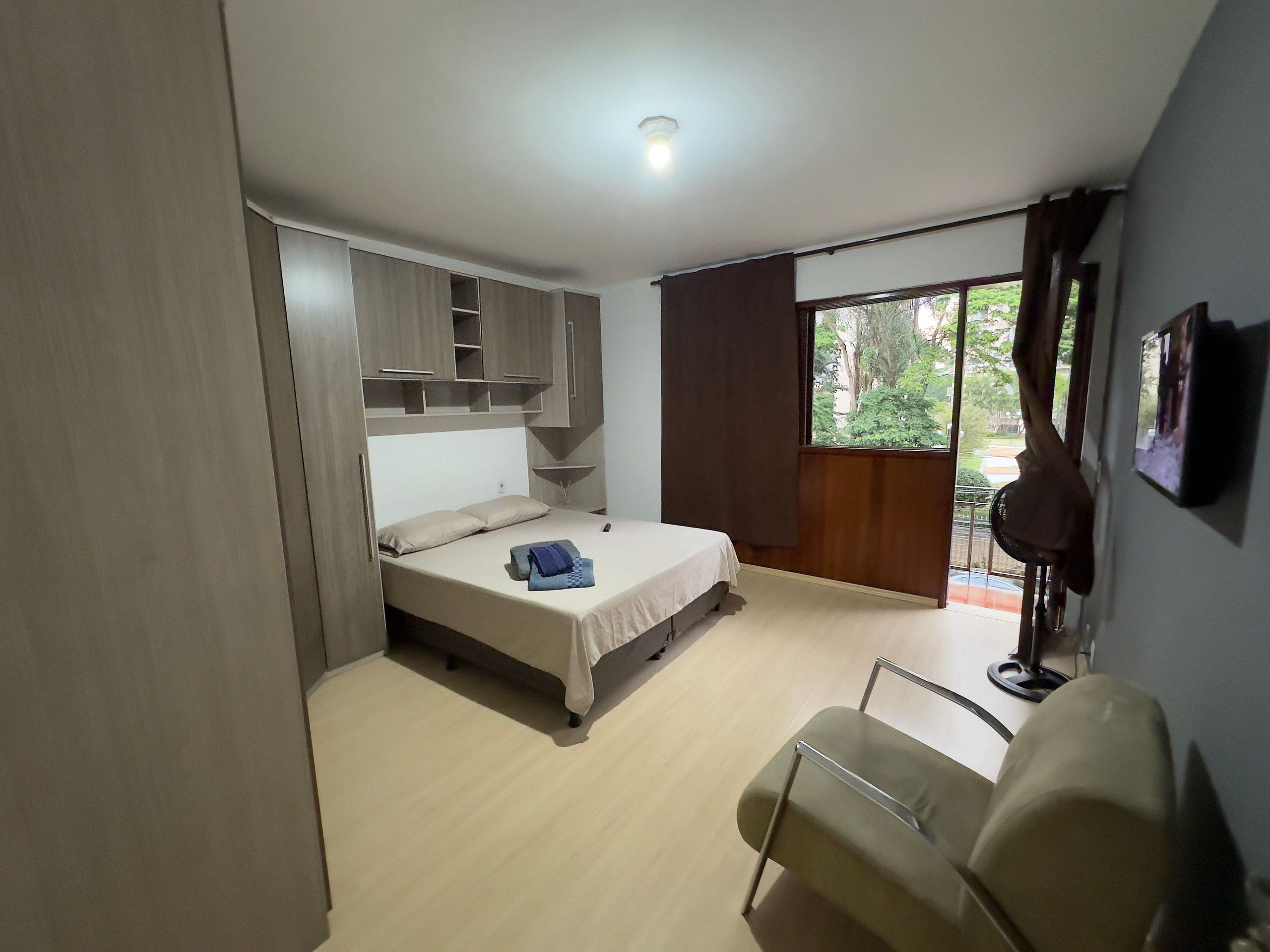 A bedroom with a bed, built-in wardrobe, a chair, and a large window.