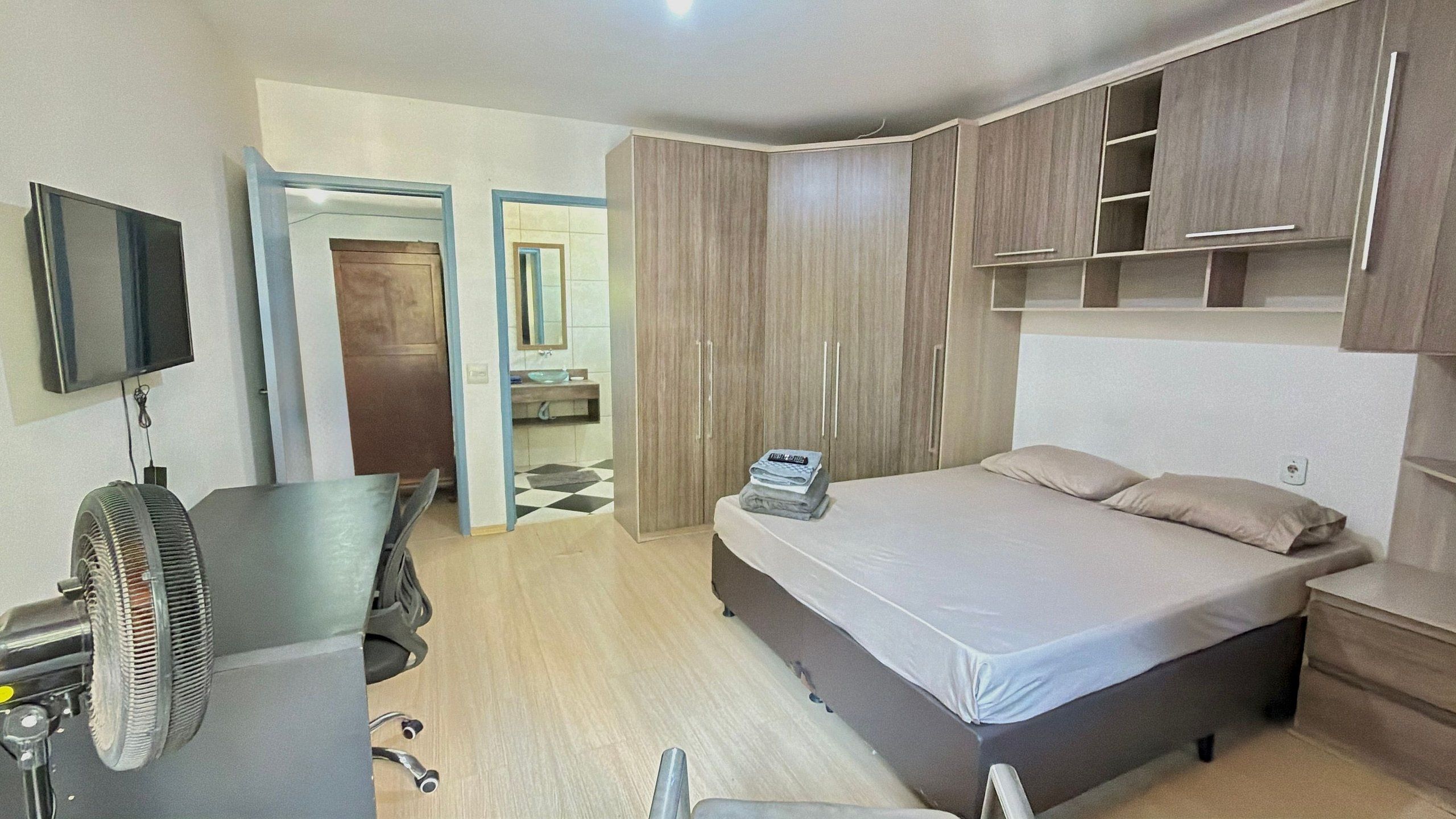 A hotel room with a bed, a desk with a chair, a TV, and a wardrobe.