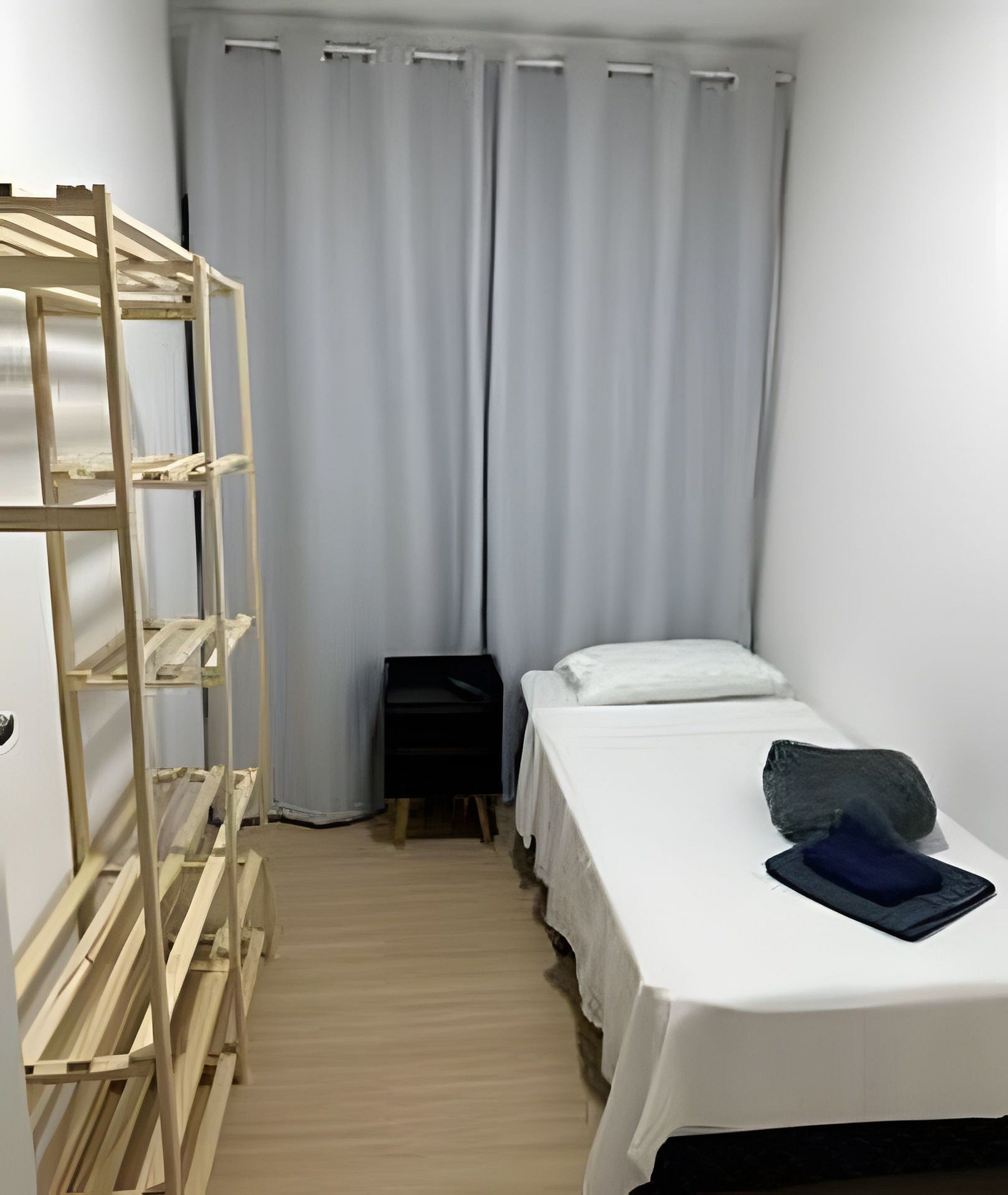 A small, single-bed room with a wooden ladder, a bedside table, and a curtain.