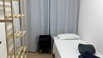 A small, single-bed room with a wooden ladder, a bedside table, and a curtain.
