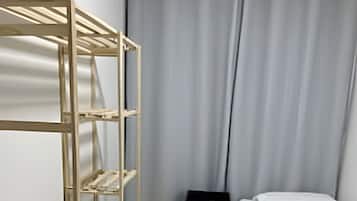 A room with a bunk bed, a wooden shelf unit, a small black table, and a white bed with a pillow.