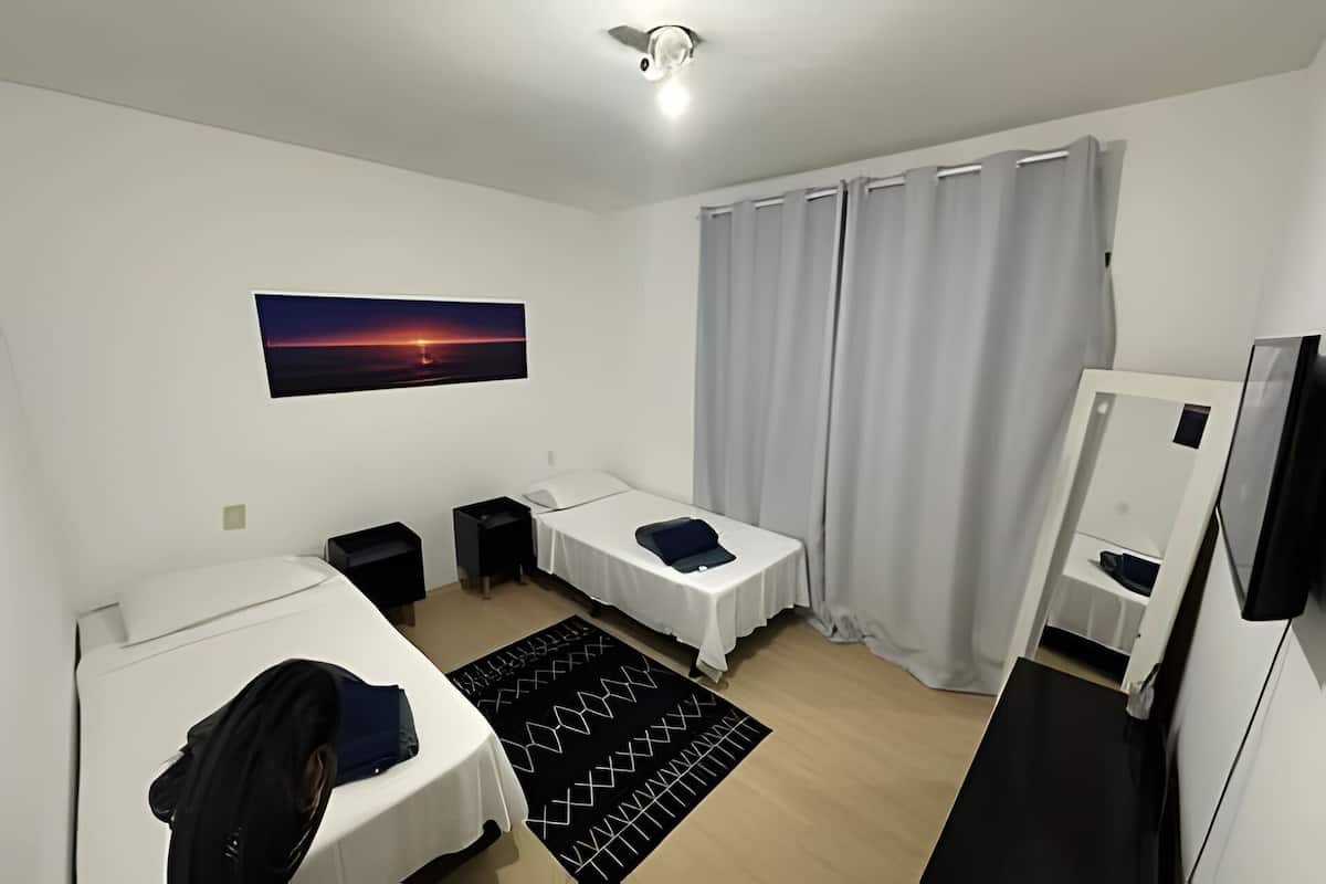 Ein Hotelzimmer mit zwei Betten, einem Schreibtisch, einem Stuhl, einem Fernseher, einem Kleiderschrank und einem Fenster mit Vorhängen.