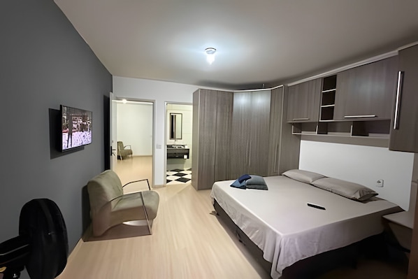 Un dormitorio moderno con cama, una silla, televisor y armario.