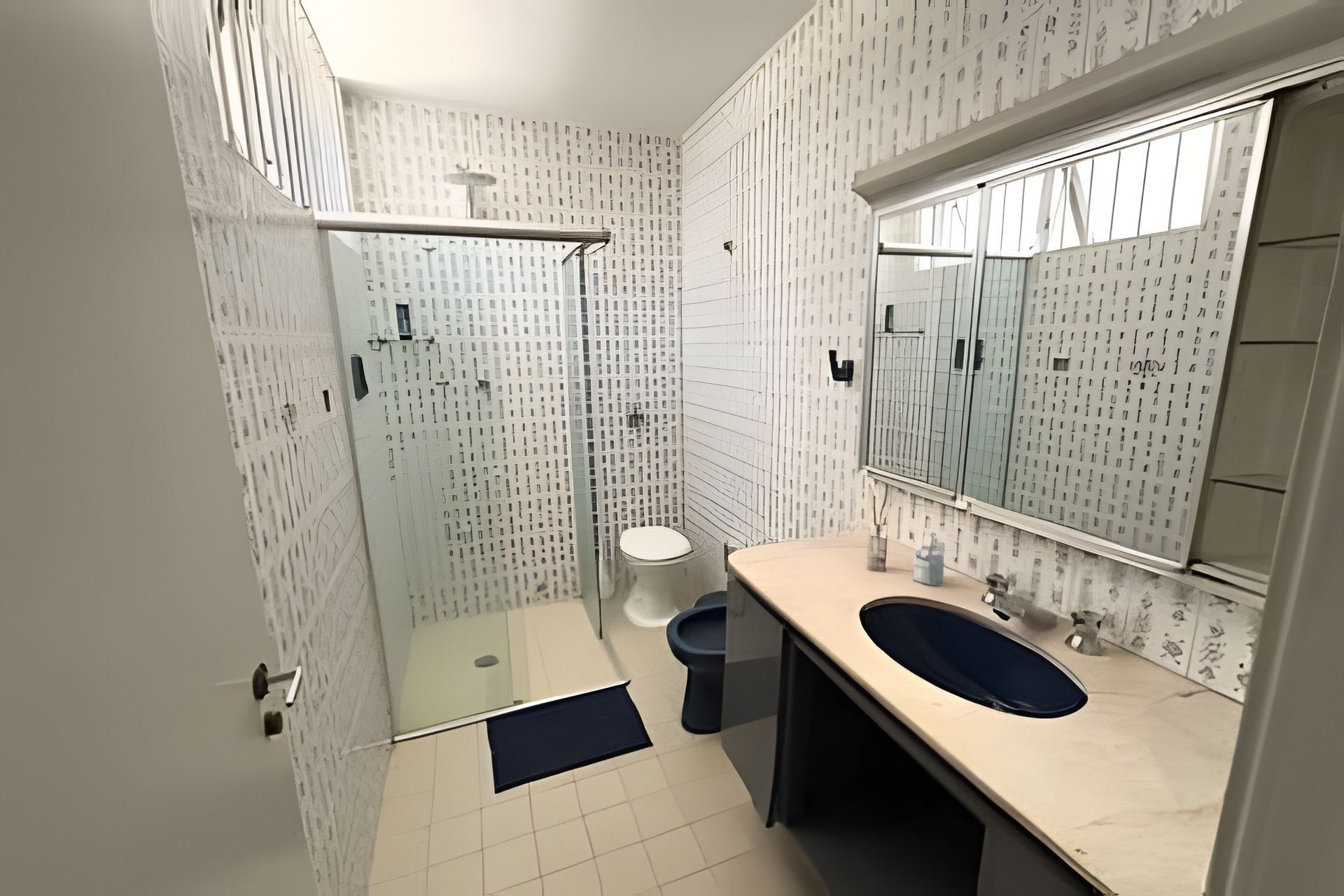 Un baño con cabina de ducha de vidrio, inodoro, lavamanos con espejo y paredes con diseño.