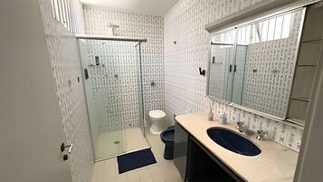 Un baño con cabina de ducha de vidrio, inodoro, lavamanos con espejo y paredes con diseño.