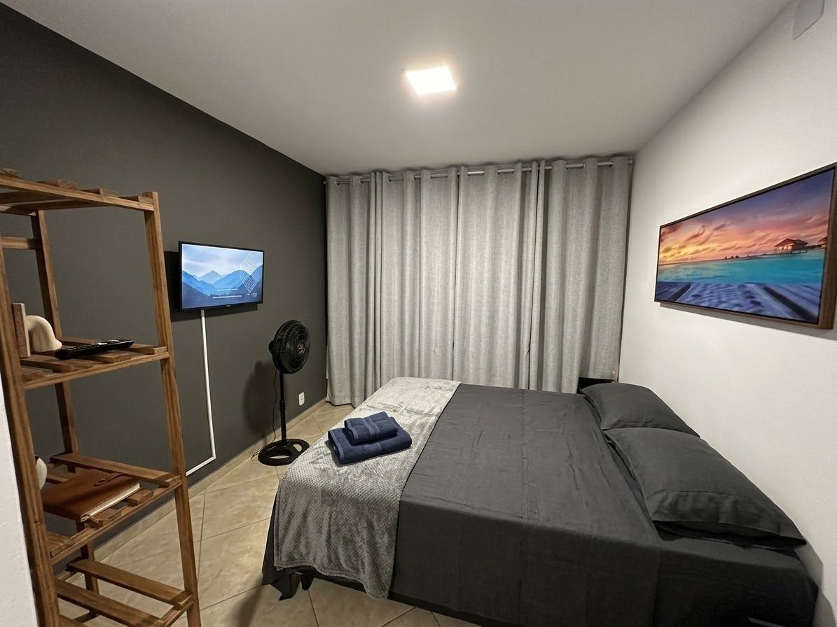 A bedroom with a bed, a television, a fan, and a painting on the wall.