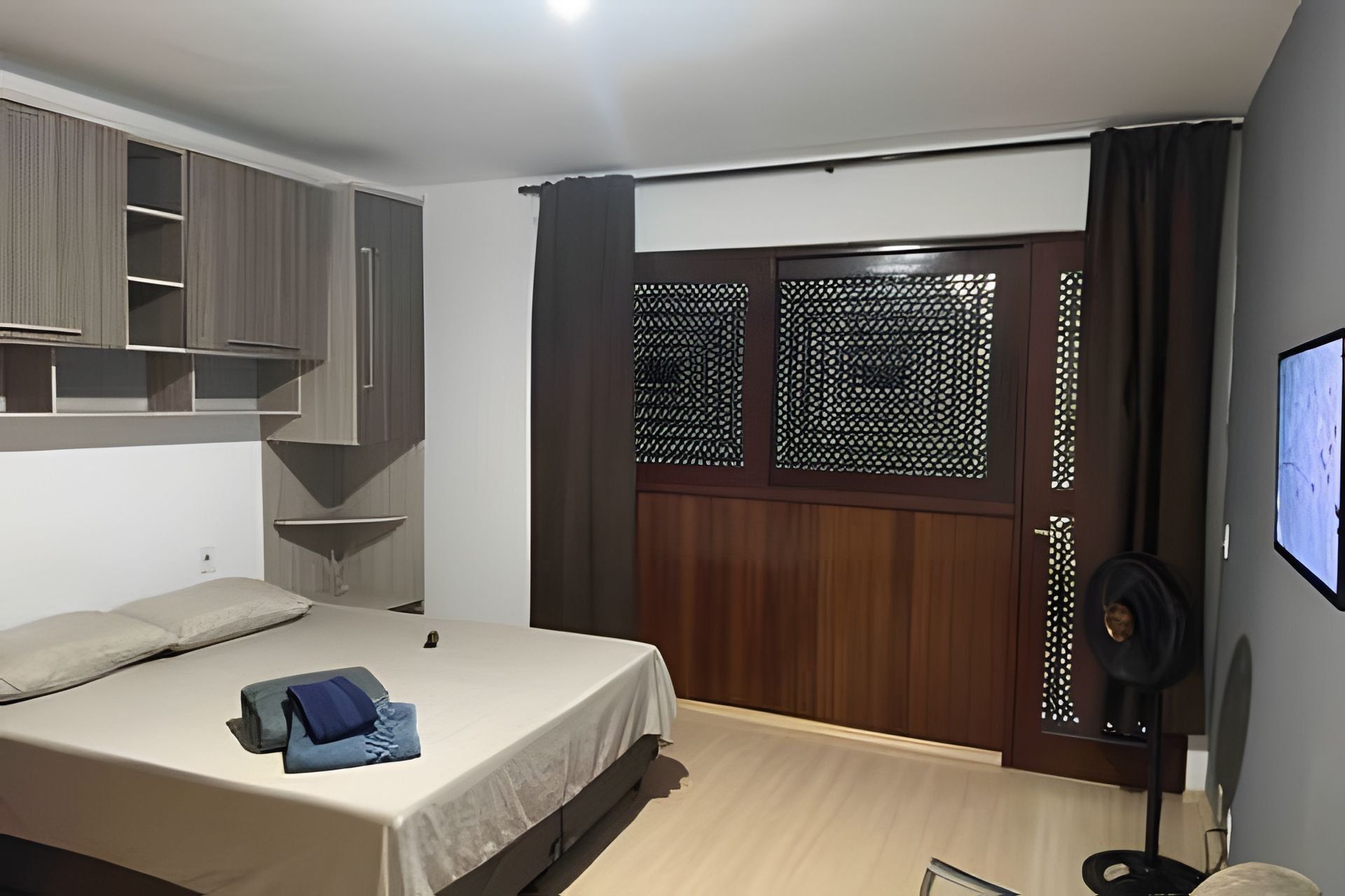 A bedroom with a bed, built-in shelving, a wardrobe, and a television.