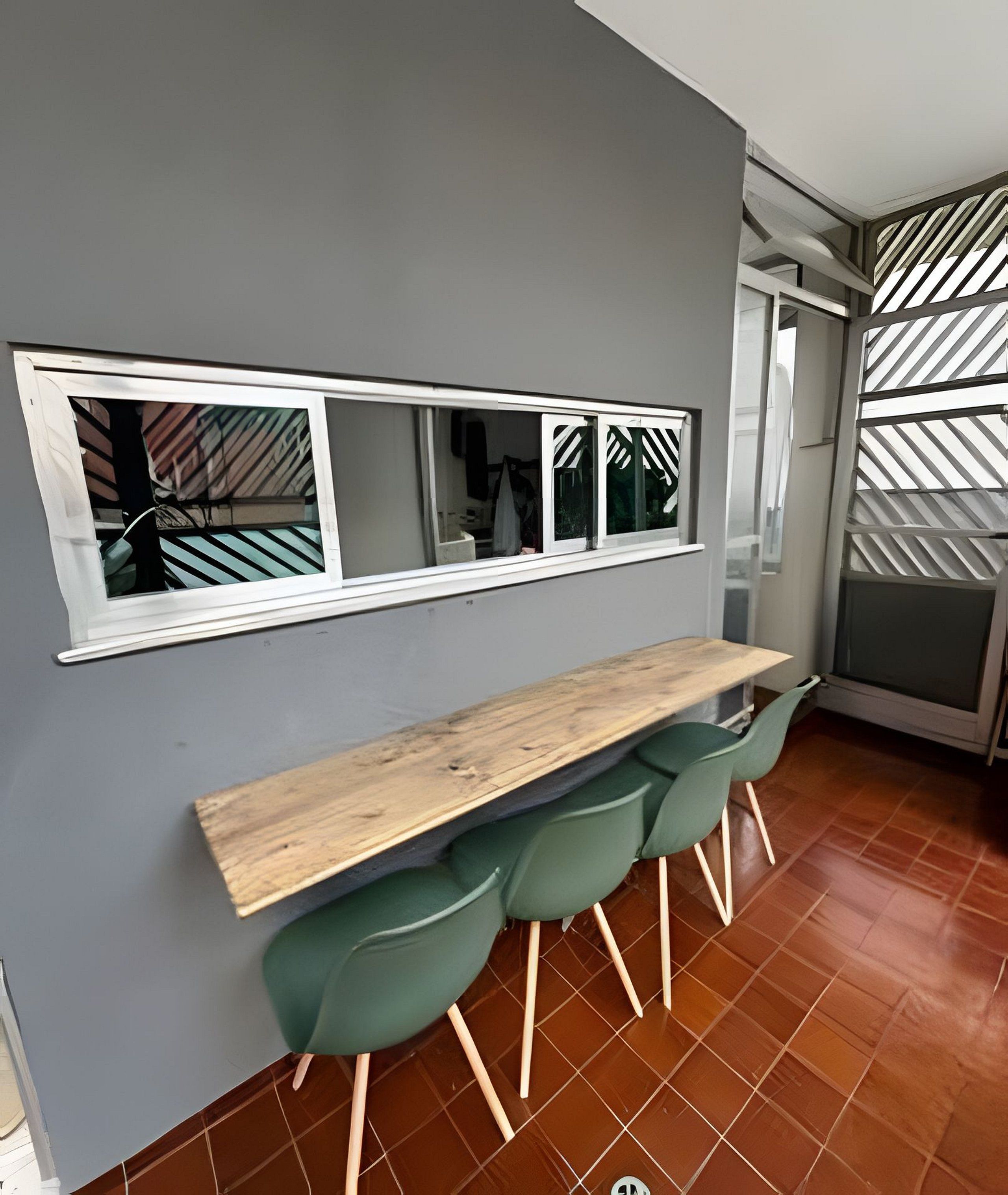 A modern kitchen with a wooden bar counter, green chairs, and a large window with a view of the outside.