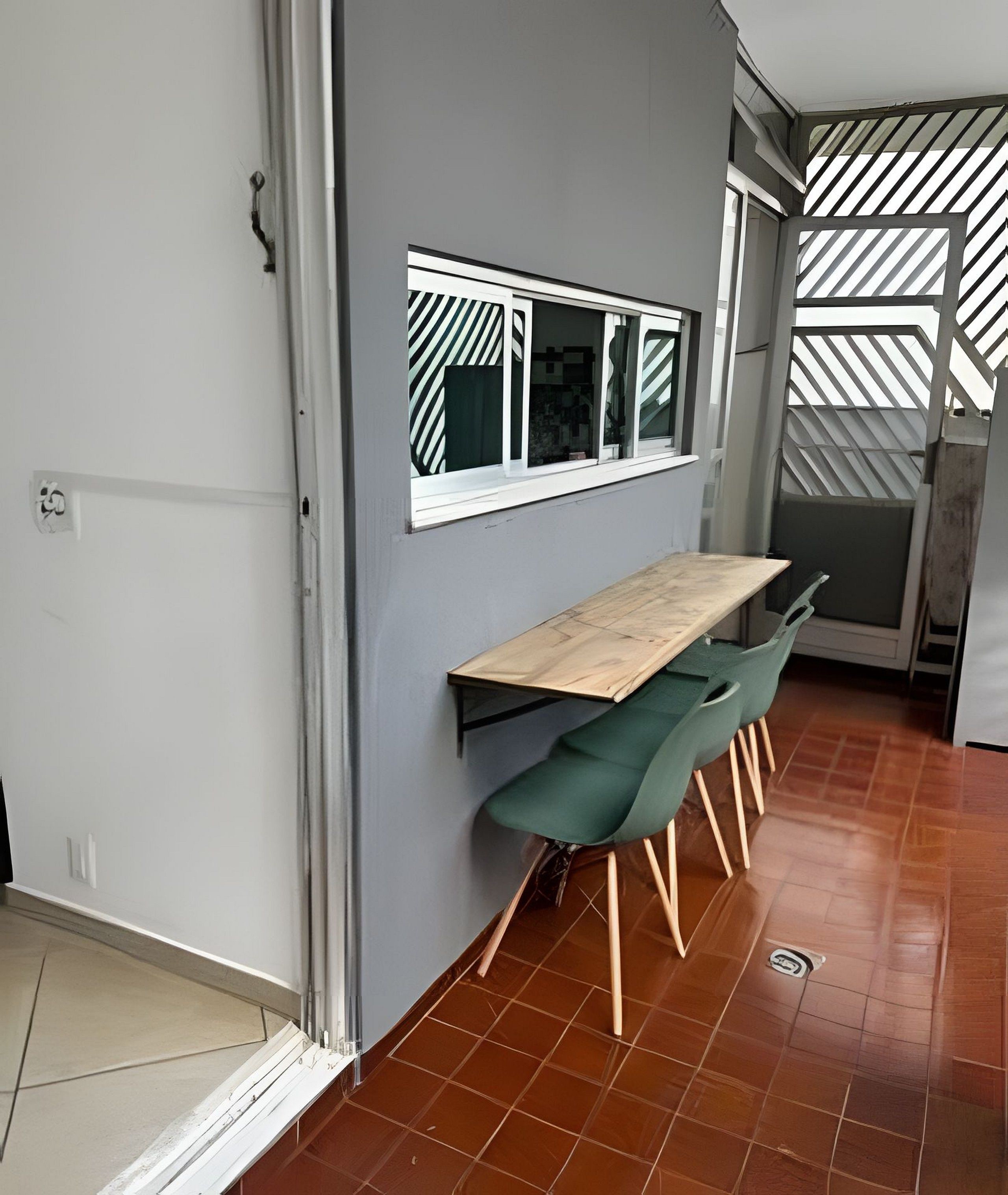 A modern kitchen with a wooden table and green chairs, a window with striped blinds, and a tiled floor.