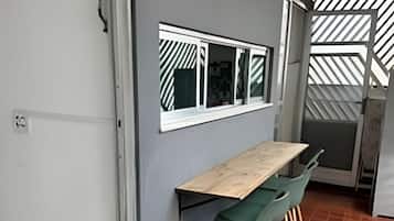 A modern kitchen with a wooden table and green chairs, a window with striped blinds, and a tiled floor.