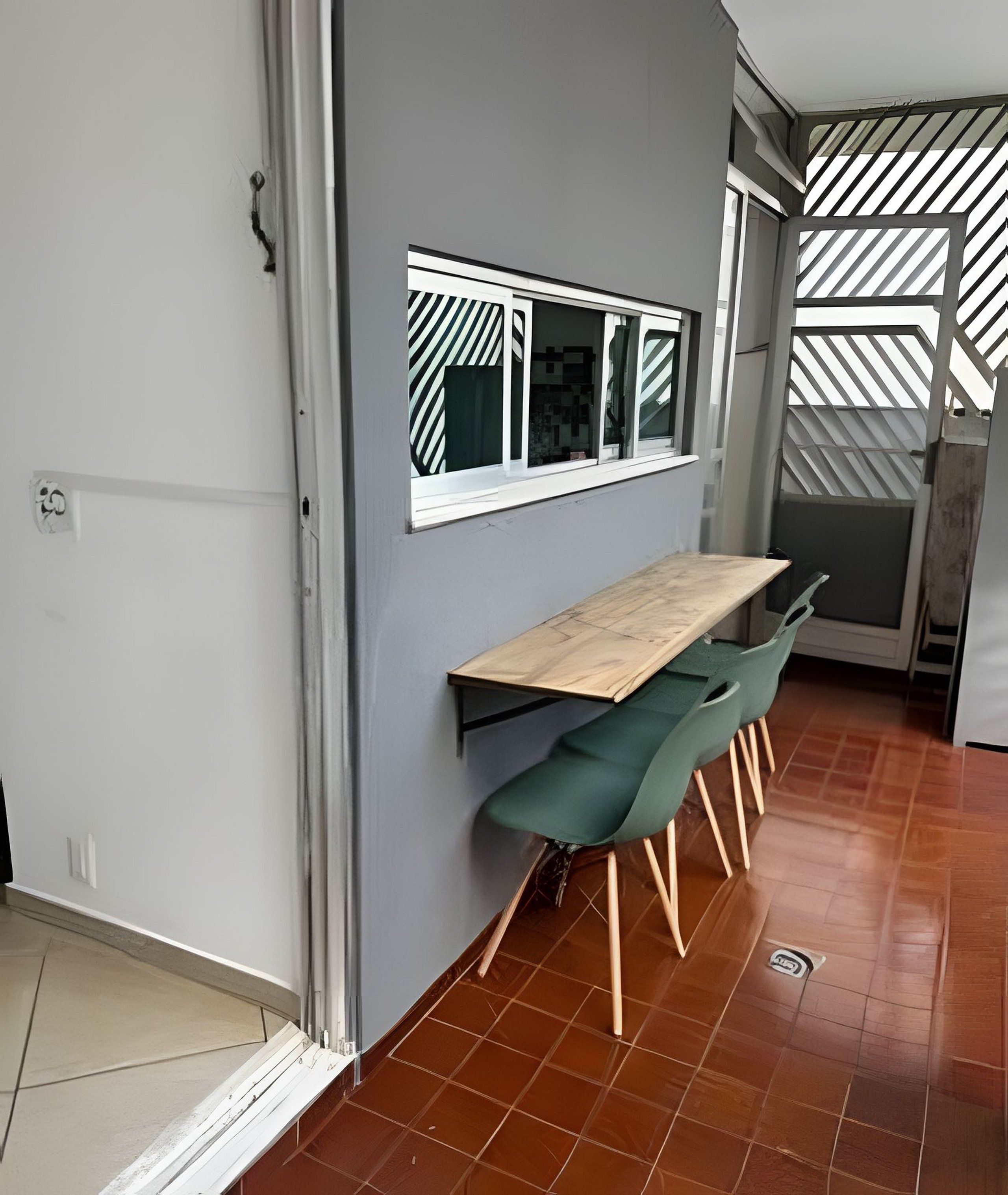 A modern kitchen with a wooden countertop, green chairs, and a patterned window.