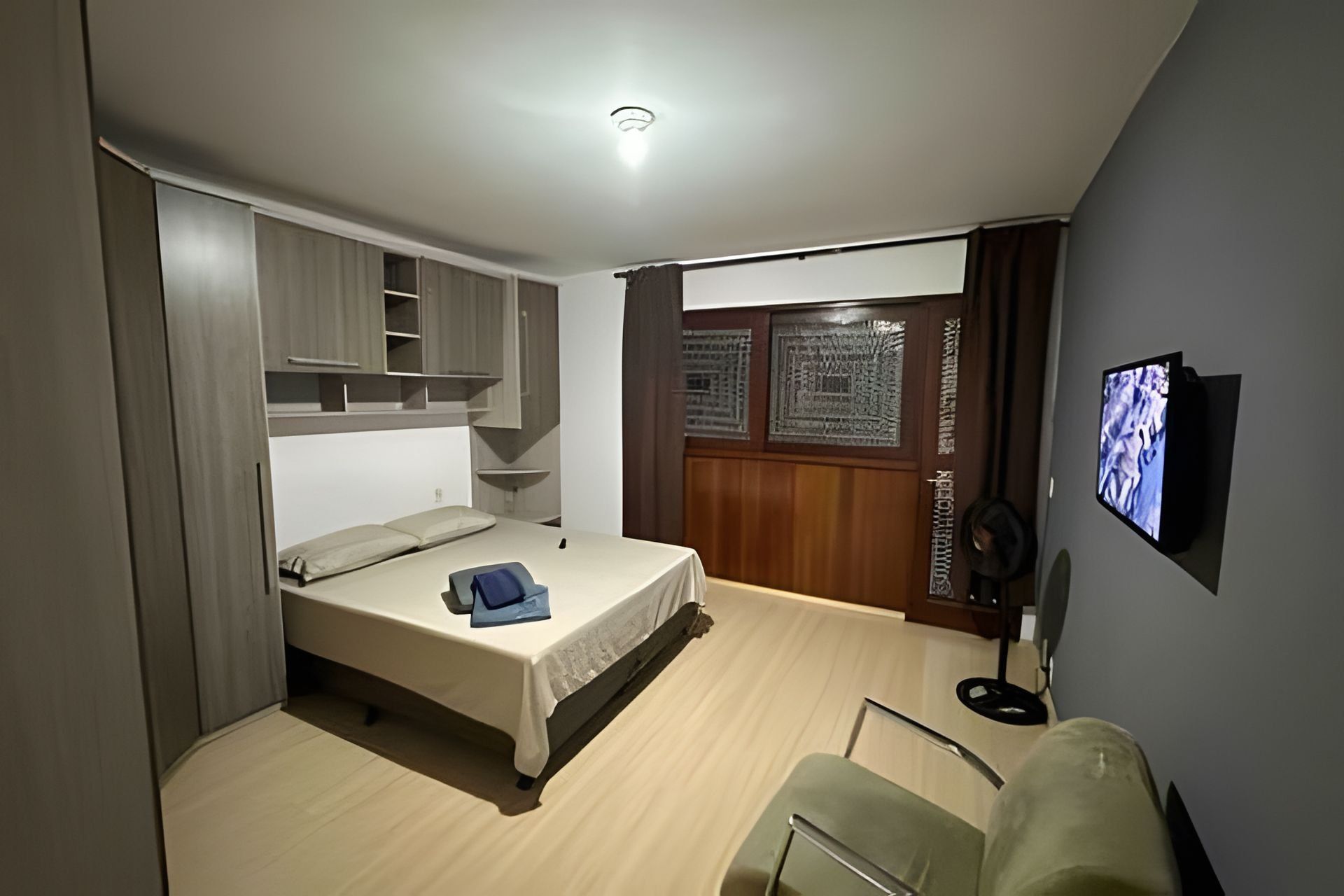 A bedroom with a bed, a TV, a chair, and a wardrobe.