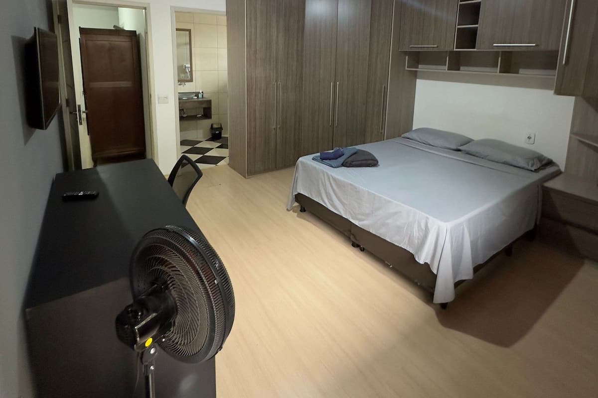 Ein Schlafzimmer mit Bett, Schreibtisch, Stuhl und Ventilator.