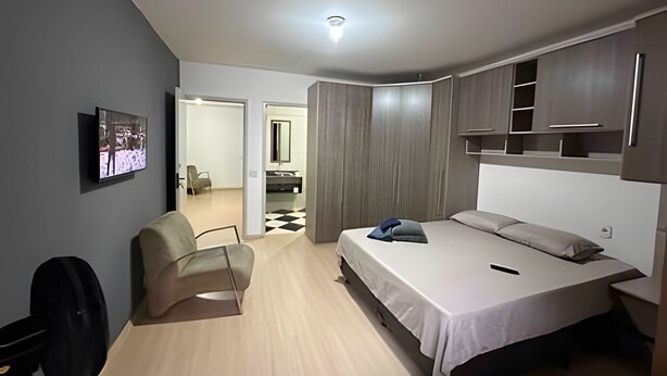 A modern bedroom with a bed, a chair, a TV, and a wardrobe. - Quartos vila olímpia 43 (São Paulo)