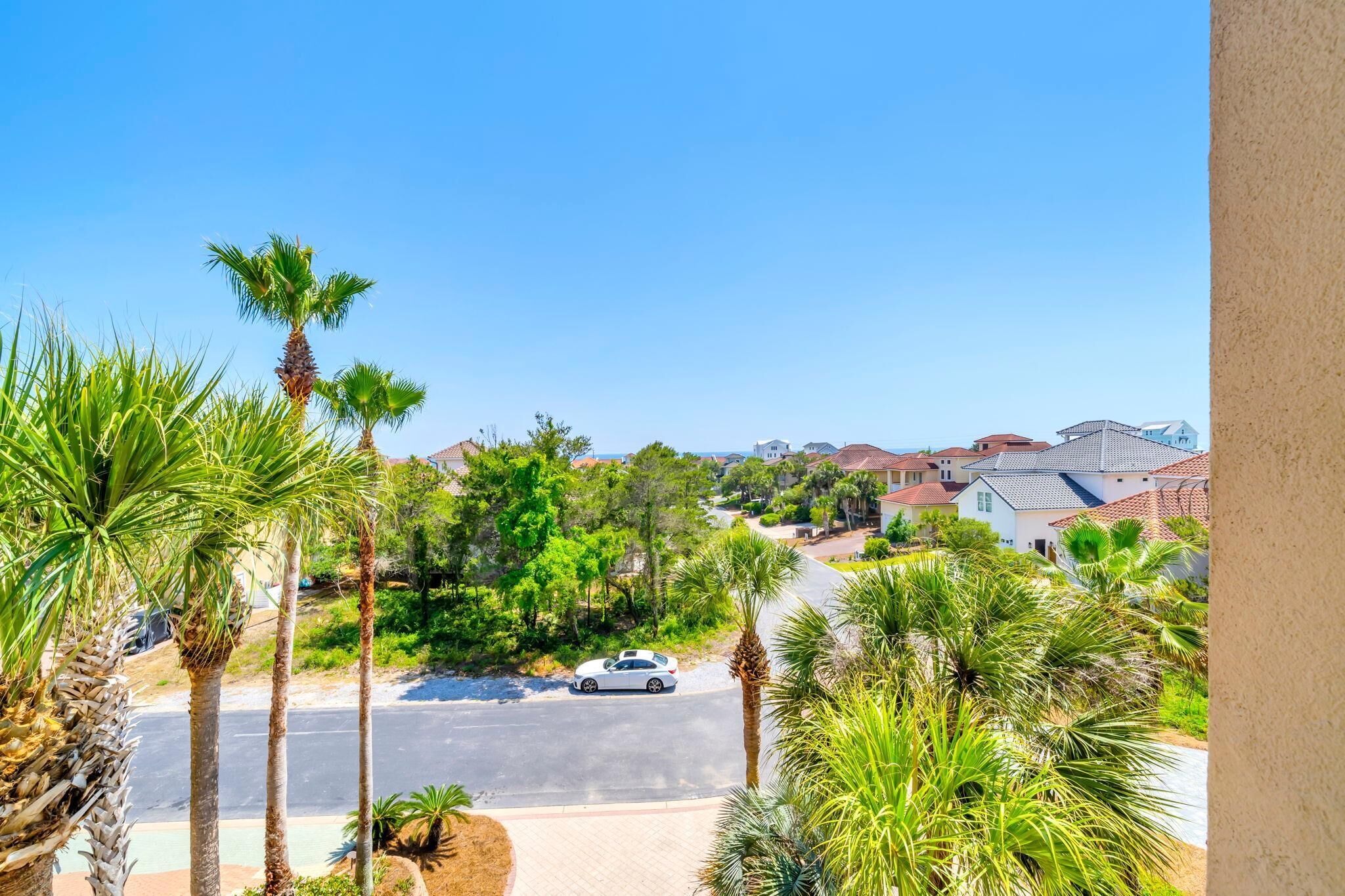 A residential street with palm trees, houses, and a car.