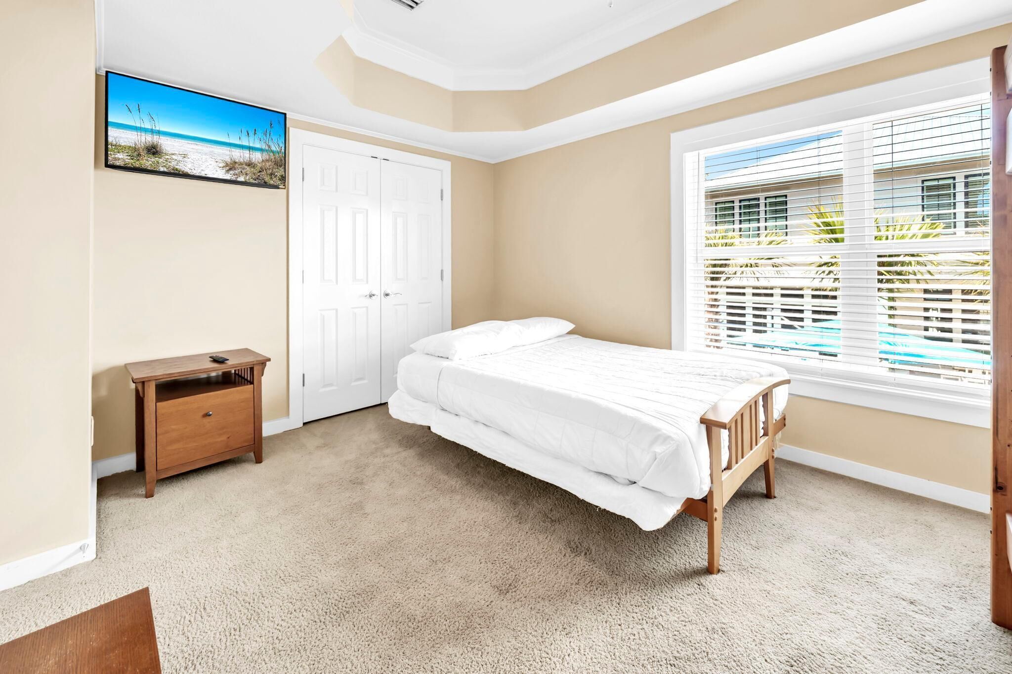 Une chambre à coucher avec un lit, une table de chevet, une porte, une fenêtre avec des stores et un tableau au mur.