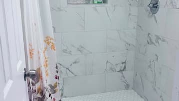 A shower with a hexagonal tile pattern, a small shelf with toiletries, and a door with a floral curtain.