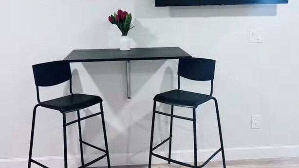 A modern room with a flat-screen TV mounted on the wall, a small table with two chairs, and a vase with flowers on the table.