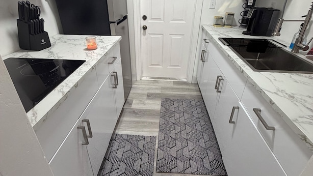 A modern kitchen with white cabinets, a microwave, a coffee maker, and a sink.