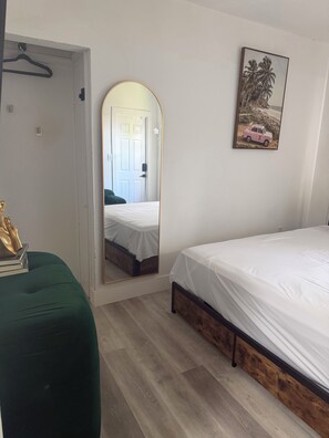 A bedroom with a bed, a green chair, a mirror, a door, and a framed picture on the wall.
