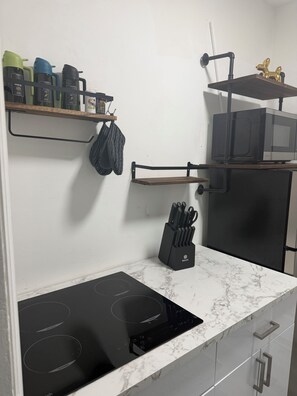 A kitchen with a black induction cooktop, a microwave, and a knife block on the counter.