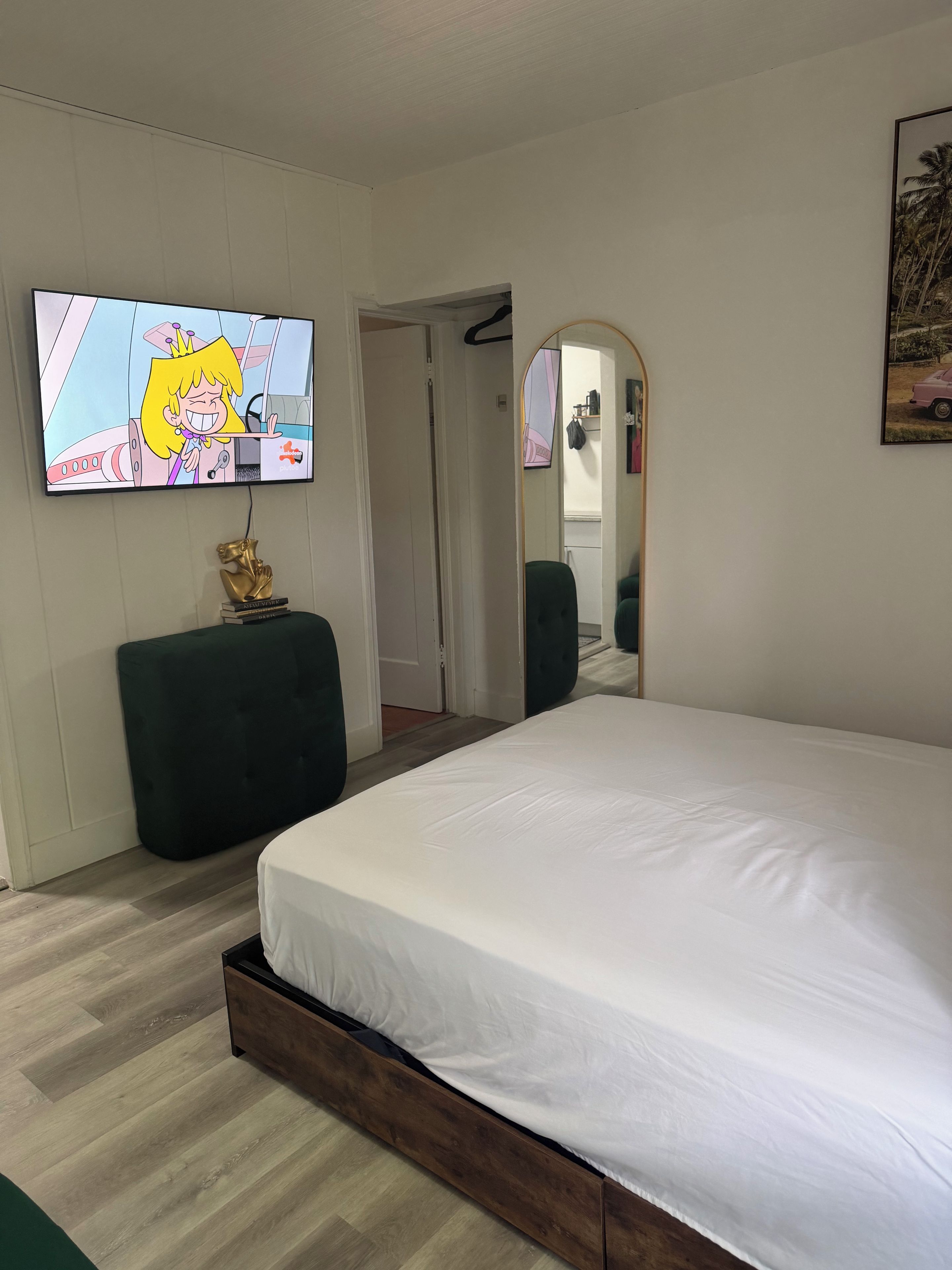 Een slaapkamer met een groot bed, een televisie aan de muur, een spiegel en een deur naar een andere kamer.