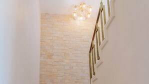 A staircase with wooden steps and white walls, leading to a room with a brick wall and a chandelier. - Royale Jazz Hotel (Kingston)