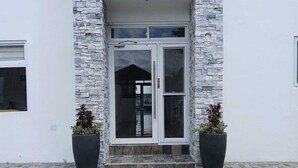 A modern building with a stone facade, a glass door entrance, and two potted plants on the ground. - Royale Jazz Hotel (Kingston)