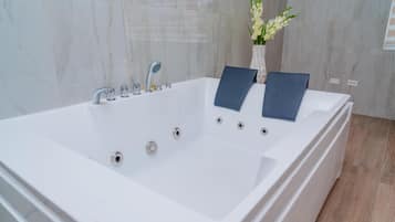 Un baño moderno con una bañera blanca grande, un florero con flores y un perchero.