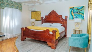 A bedroom with a wooden bed, a desk, a chair, and artwork on the walls. - Royale Jazz Hotel (Kingston)