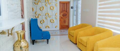 A hallway with a white brick wall, a blue chair, a yellow sofa, and a patterned wall.