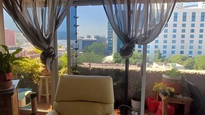 Una habitación con vistas a un paisaje urbano, una silla y plantas en macetas.