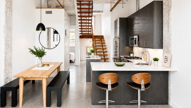 Une cuisine moderne dotée d’un îlot central, de tabourets de bar, d’un banc en bois et d’un escalier menant à un niveau supérieur.